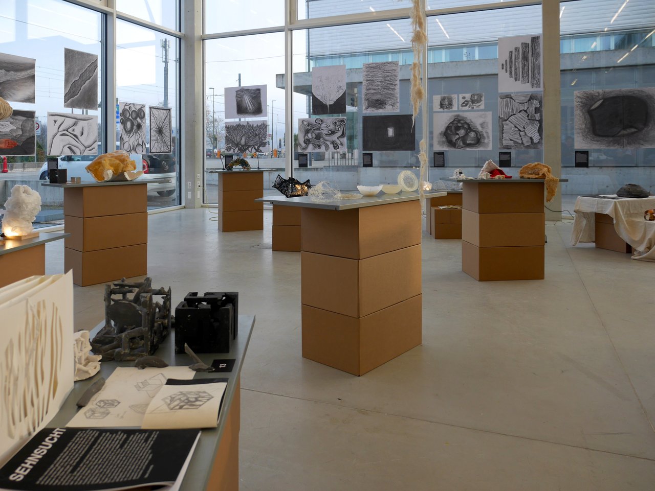 Ausstellung in einer modernen Galerie mit Kunstobjekten, Zeichnungen und Skulpturen auf erhöhten Podesten