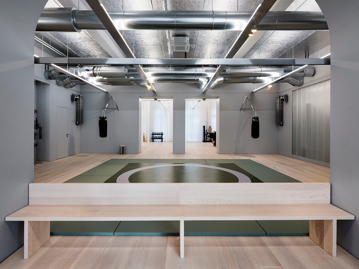 Modernes Fitnessstudio-Interieur mit sichtbarer Technik, Sportausrüstung und einer langen Holzbank im Vordergrund
