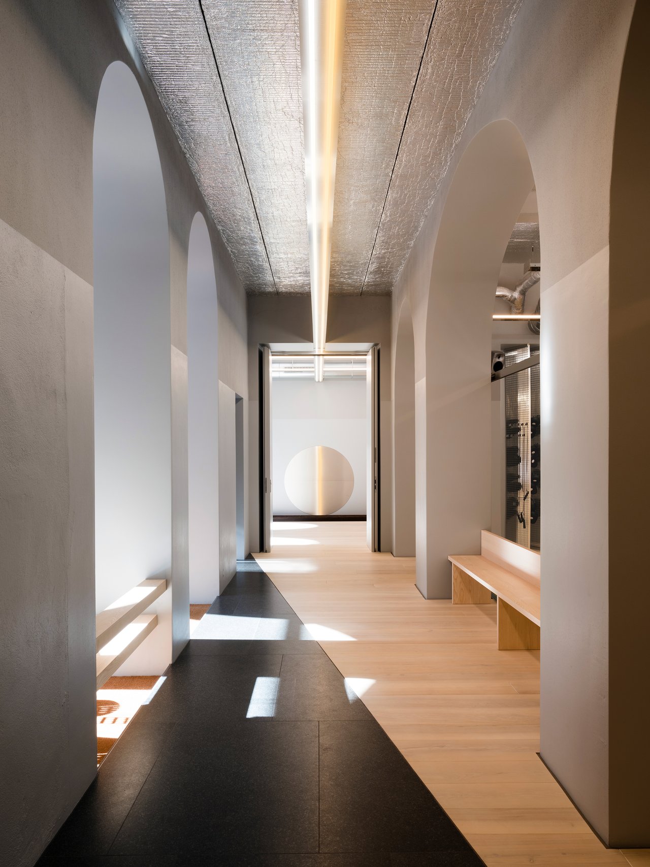 Architektonische Innenaufnahme eines modernen Flurs mit Rundbögen, Holzfußboden und langer, linearer Beleuchtung.