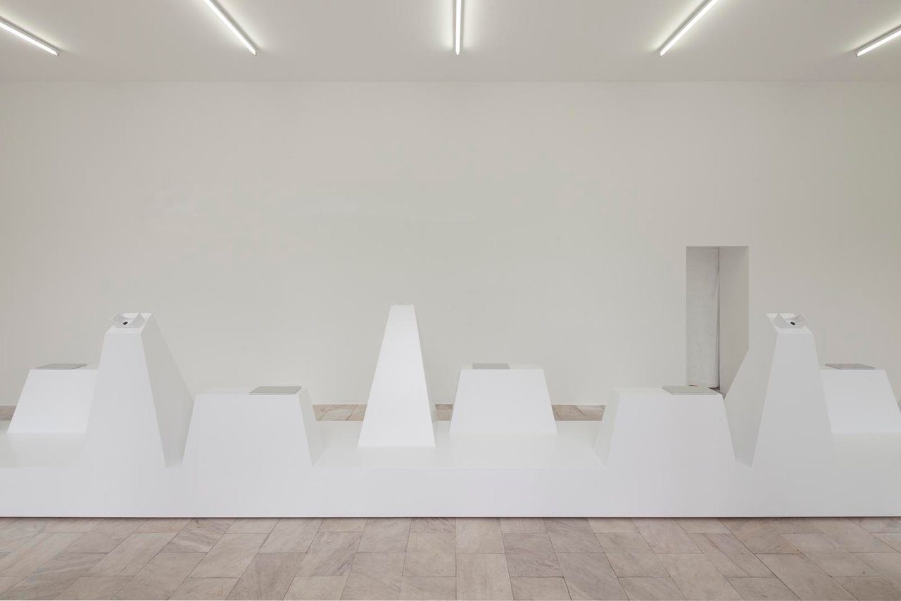 Minimalistische Kunstausstellung mit weißen, geometrischen Skulpturen und Spotbeleuchtung in einem leeren Galerieraum