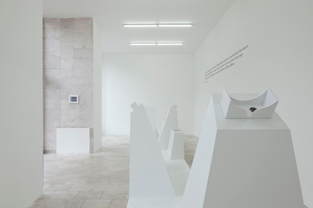 Moderne Kunstausstellung in einer hellen Galerie mit minimalistischen Skulpturen und weißem Sockel