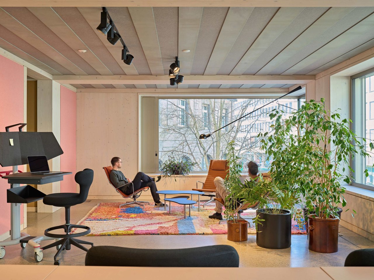 Modernes, helles Büro mit Pflanzen, Sitzgelegenheiten und zwei Personen, das ein entspanntes Arbeitsumfeld darstellt.