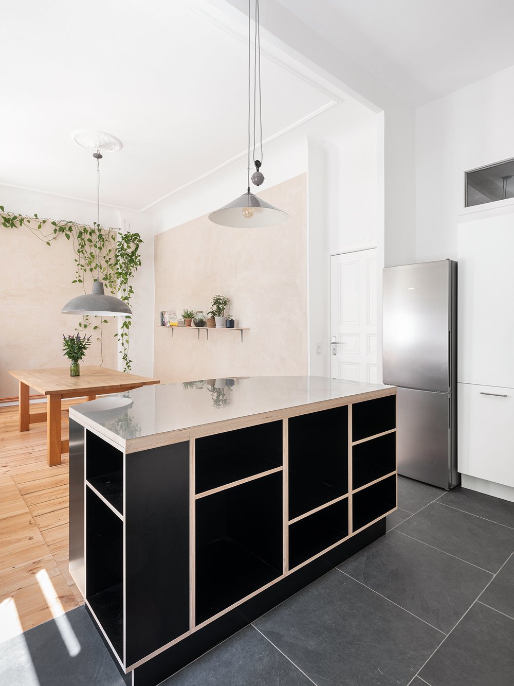 Moderne Kücheninsel mit schwarzer Front und weißer Arbeitsplatte in einem hellen Wohnraum