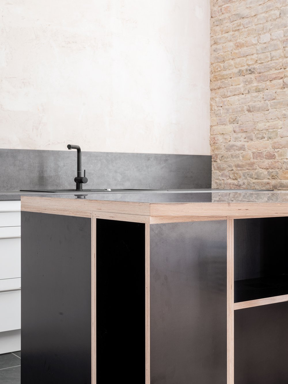 Modernes Küchen- oder Waschbeckenmöbel mit dunkler Front und Holz-Akzenten, vor einer hellen Wand und einem Backsteinmauerwerk